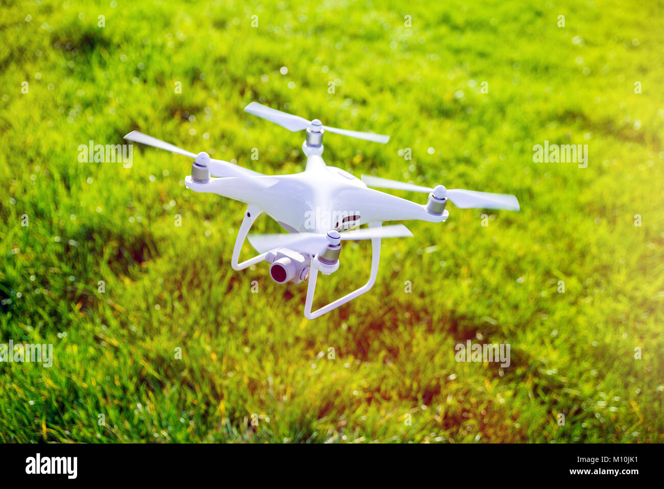 Foto di un flying bianco quadcopter professionale drone telecamera con erba verde in background Foto Stock