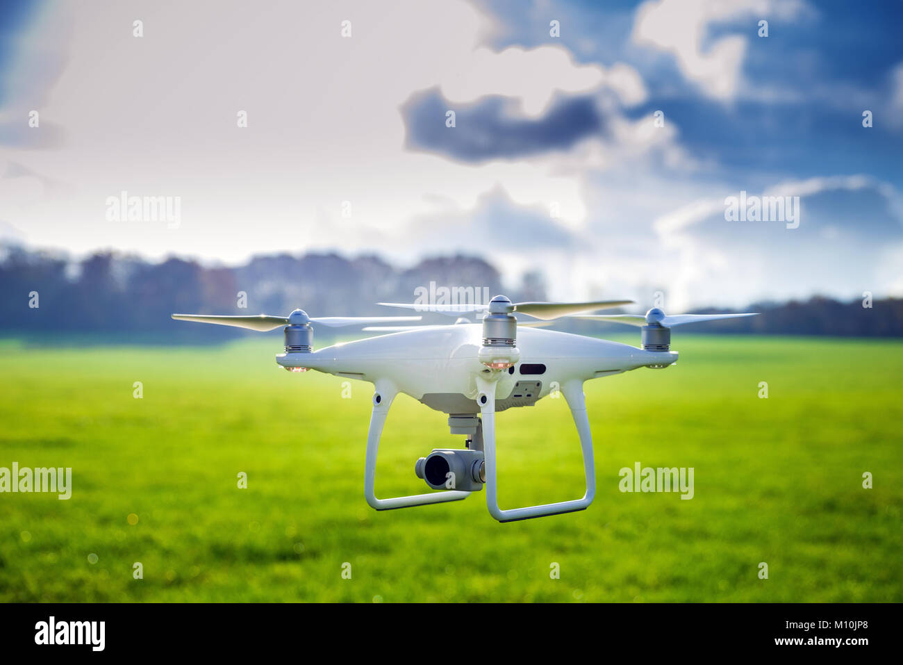 Foto di un flying bianco quadcopter professionale drone fotocamera nella parte anteriore di erba verde e foresta Foto Stock