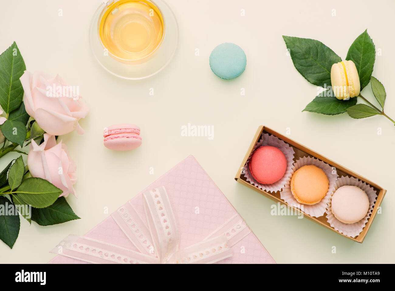 Amaretti colorati e rose fiori con tè sul verde chiaro. Dolce macarons in confezione regalo. Vista superiore Foto Stock