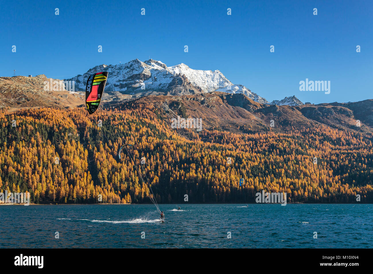 Wind surf sul lago di Silvaplana con la caduta delle foglie colore in larice alberi in Engadina, Graubuden, Svizzera, Europa. Foto Stock