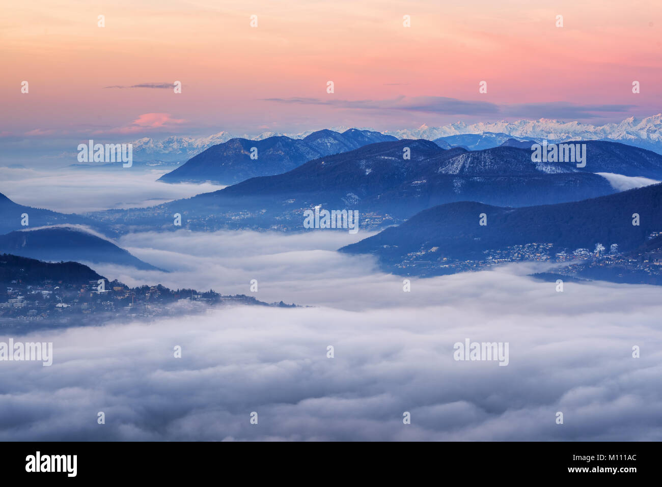 Bellissima vista sul lago di Lugano e sulle Alpi svizzere coperto di nuvole su sunrise, Svizzera Foto Stock
