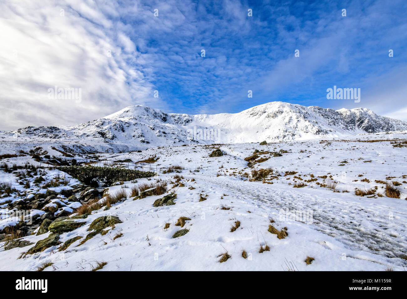 Bella scena invernale del ponte in pietra sopra la beck sulla cicatrice Walna road tra Coniston e la Duddon Valley con la coperta di neve Dow Crag rid Foto Stock