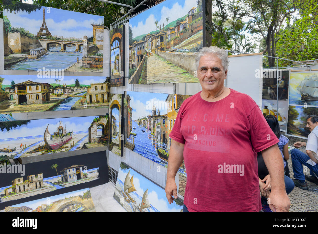 Brasiliano caucasica uomo vendita di paesaggio e paesaggi dipinti ad olio ad una strada del mercato di Belo Horizonte, Minas Gerais, Brasile Foto Stock