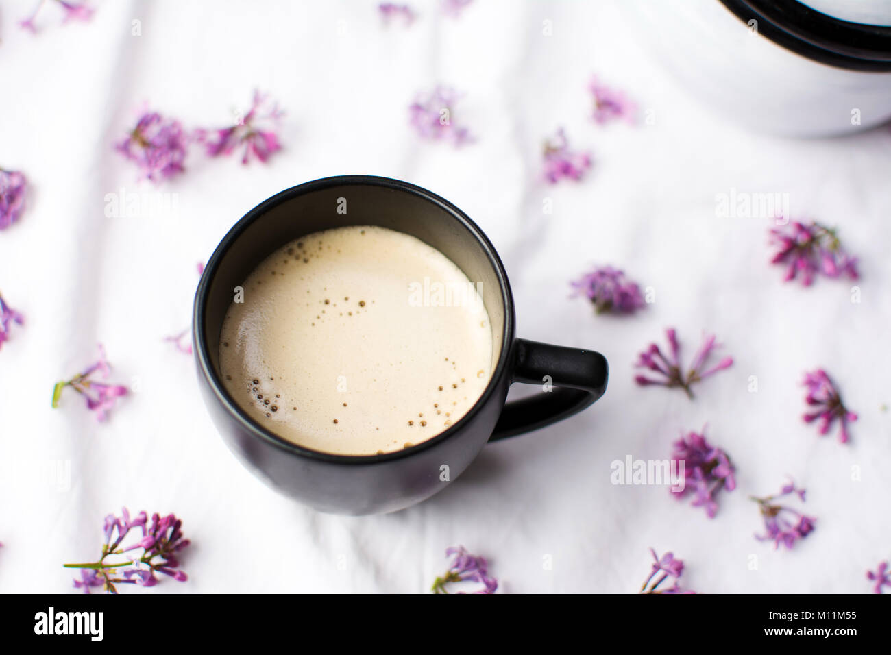 Tazza di caffè con il latte su un tavolo coperto di fiori viola Foto Stock