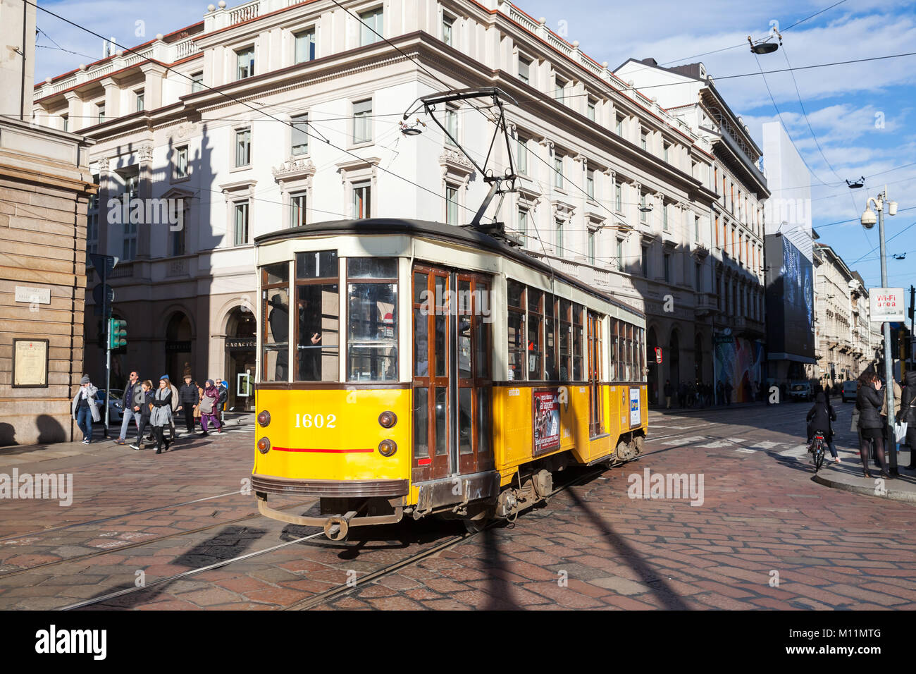 Milano, Italia - 19 Gennaio 2018: tram giallo con passeggeri va sulla strada, in vista posteriore La gente comune a piedi nelle vicinanze Foto Stock