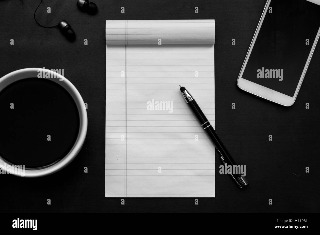Scrivania nera con caffè in tazza bianca, notebook, bianco smartphone e penna laici piana/ concetto di area di lavoro con il bianco e nero Foto Stock