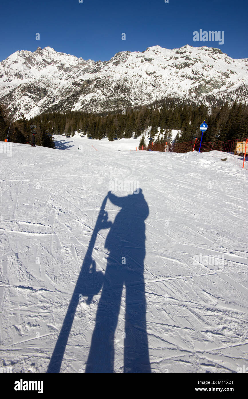 Ombra di uno snowboarder sulla pista di sci con la montagna in background Foto Stock