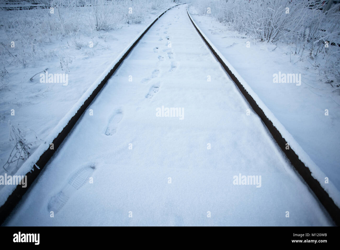 I binari della ferrovia in inverno con passi sulla neve portando avanti Foto Stock