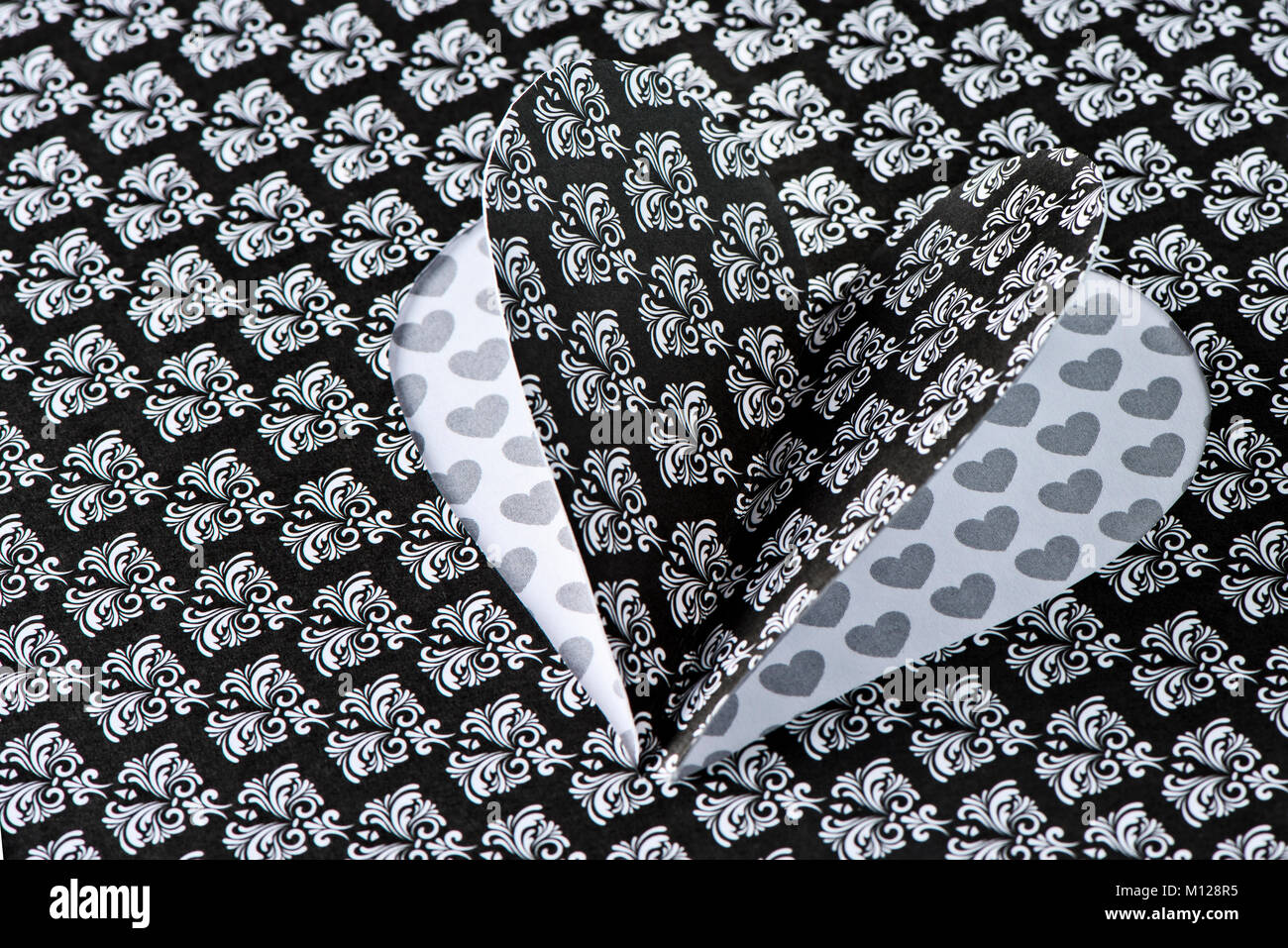 Primo piano di un cuore che si è ritagliata su un nero e bianco fiore-carta modellata con un cuore modellato sullo sfondo si vede attraverso il taglio fuori spazio Foto Stock