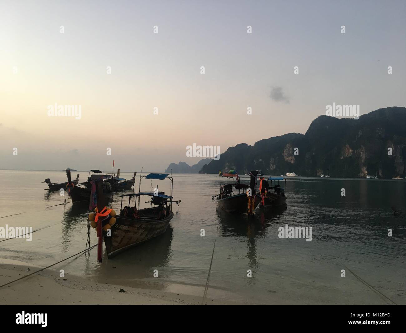 Longtailboats a fuoco sulle rive di acque cristalline e spiagge di sabbia bianca dell'isola, con il sorgere del sole in background Foto Stock