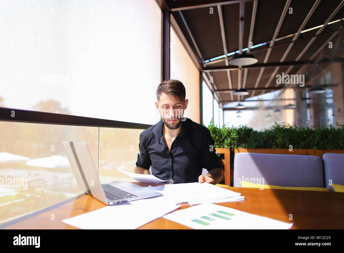 Lavoratore di ufficio ordinamento di carte sul tavolo vicino al computer portatile. Foto Stock