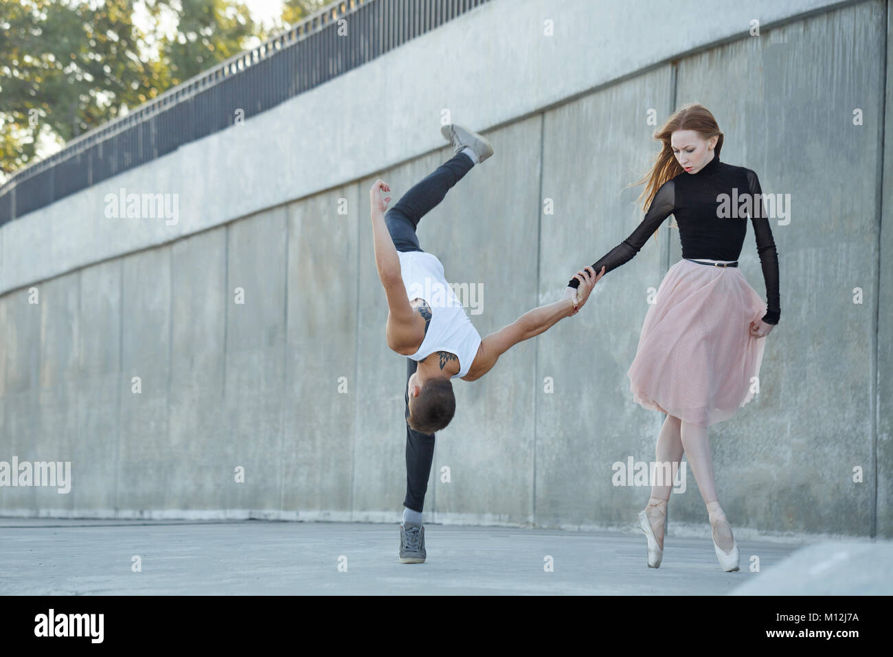 Una giovane ballerina e un uomo parkour danza nelle strade della città. La bambina sta tenendo il ragazzo con la mano. Egli capovolge in avanti. Un insolito matura in Foto Stock