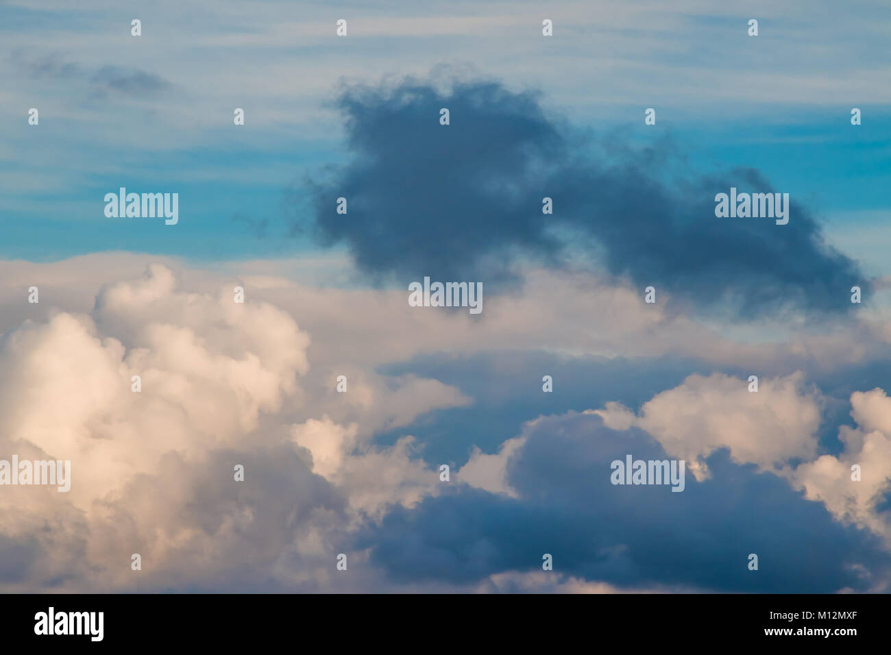 Un ciuffo di nuvole scure circondato da soffici nuvole contro un cielo blu e giallo sole del mattino Foto Stock