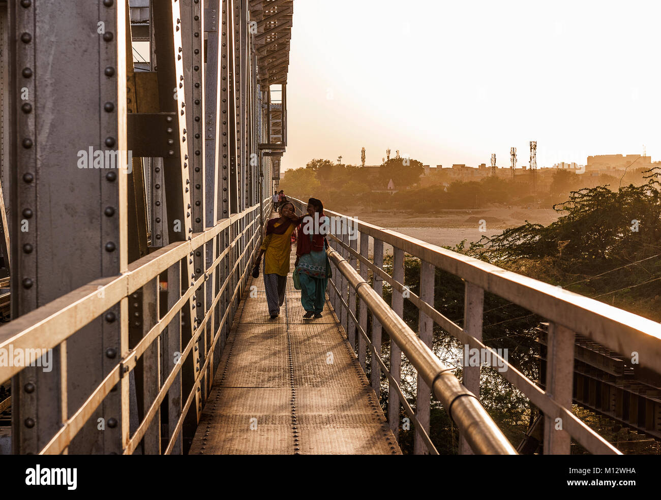 Due ragazze a piedi in ponte ferroviario dopo il lavoro sulla loro strada di casa al tramonto, Agra, India Foto Stock