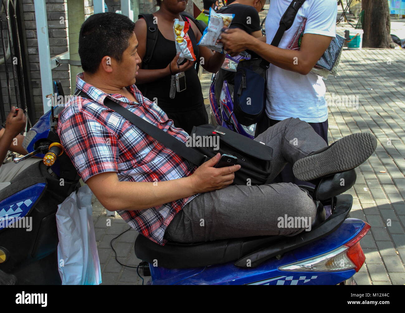 Xi'an, Cina - Cinese lavoratore di ufficio si siede sul suo scooter in strada per la sua pausa pranzo,immagine in formato orizzontale Foto Stock