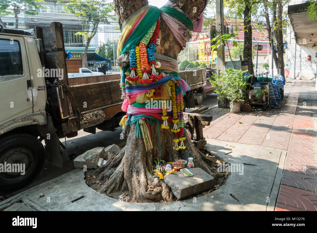 Alcuni tessuti colorati e un piccolo altare su un albero in una strada a Bangkok Foto Stock