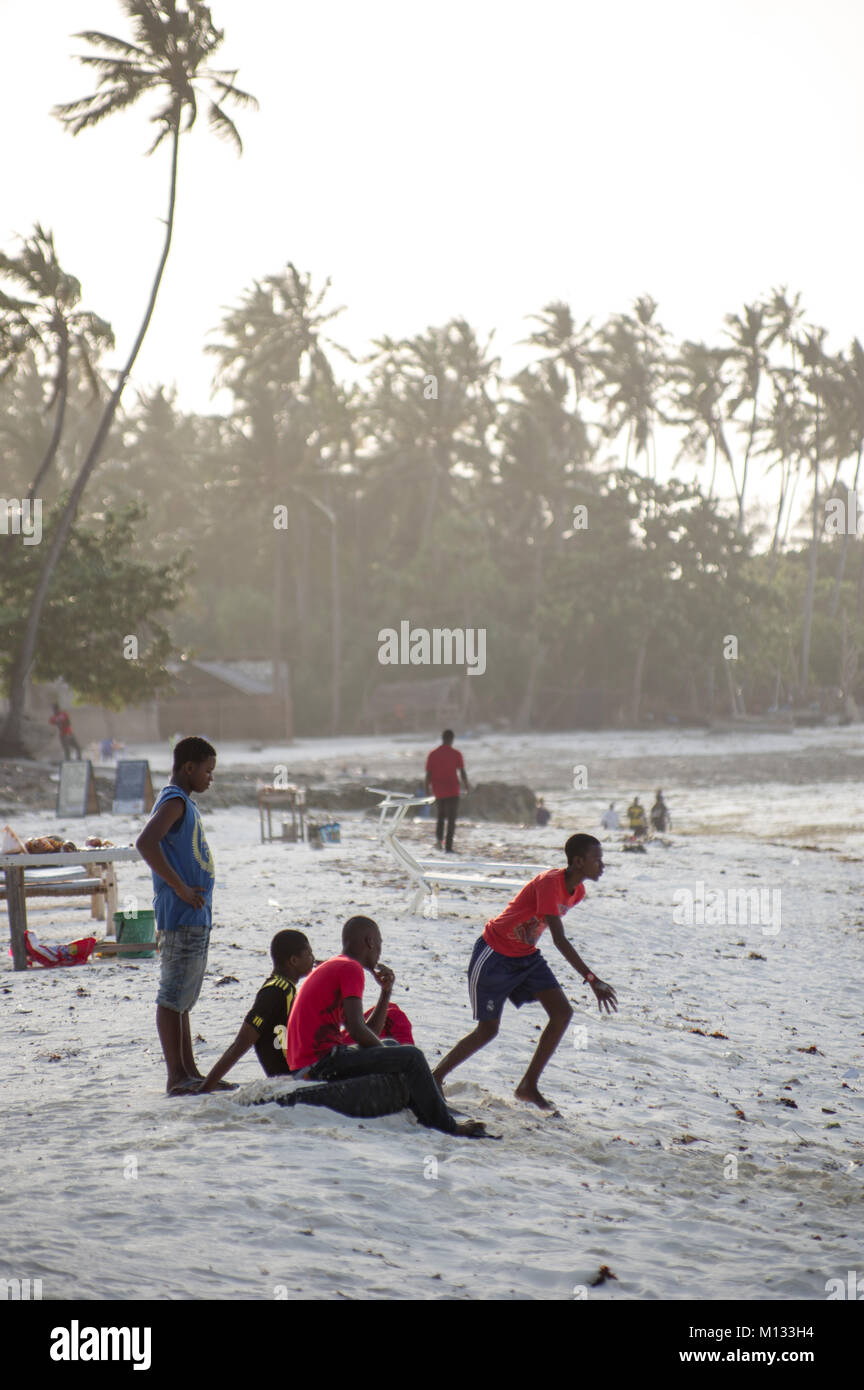 Locale di giovani tanzaniani rilassante sulla spiaggia di Nungwi, Zanzibar, giocando a calcio nel sole di setting con barche Dhow in background e la luce morbida Foto Stock