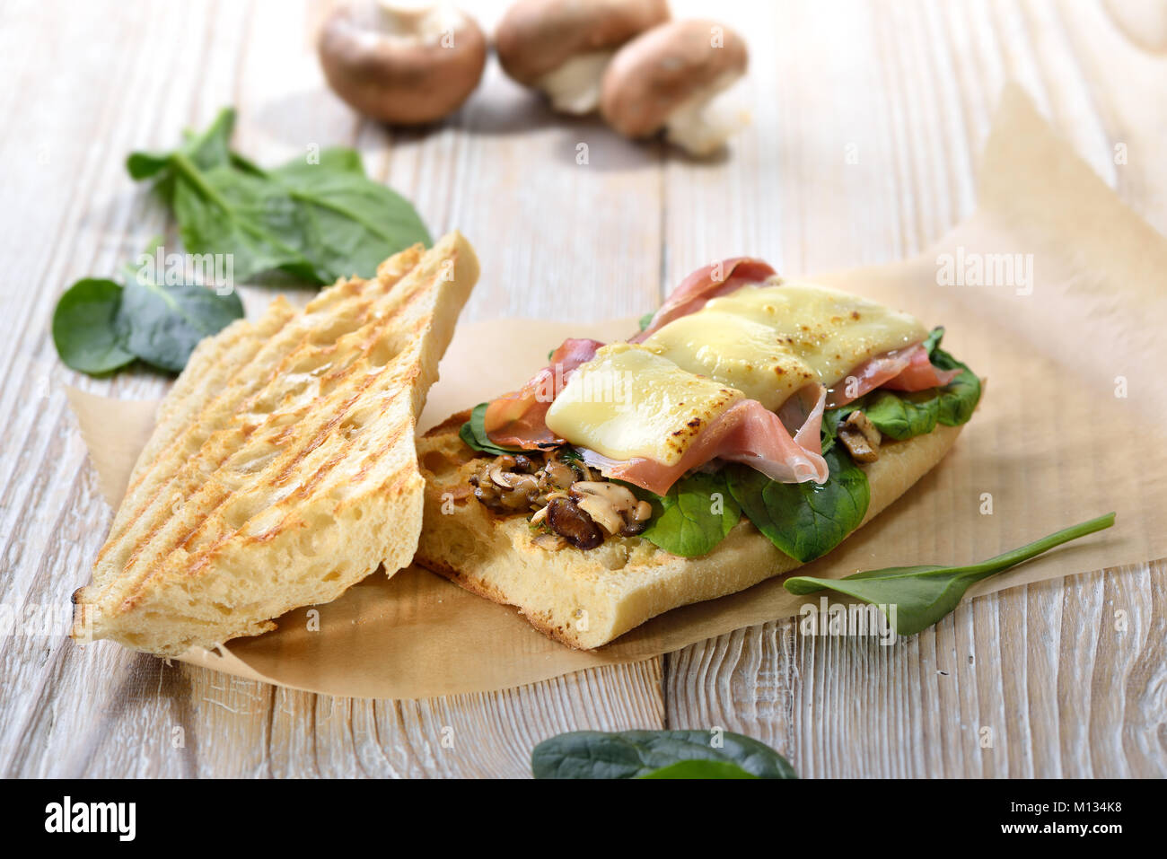 Cucina di strada: panini caldi con lo spagnolo prosciutto Serrano e giovani foglie di spinaci conditi con formaggio grattugiato servito su un sfondo di legno Foto Stock