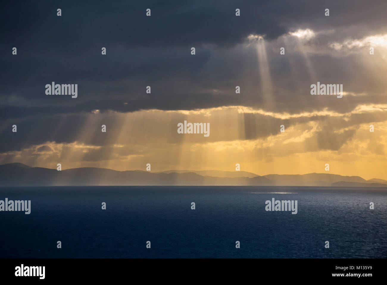 Sunray scoppio attraverso il foglio denso di pioggia nuvole sopra l'acqua di mare al tramonto Foto Stock