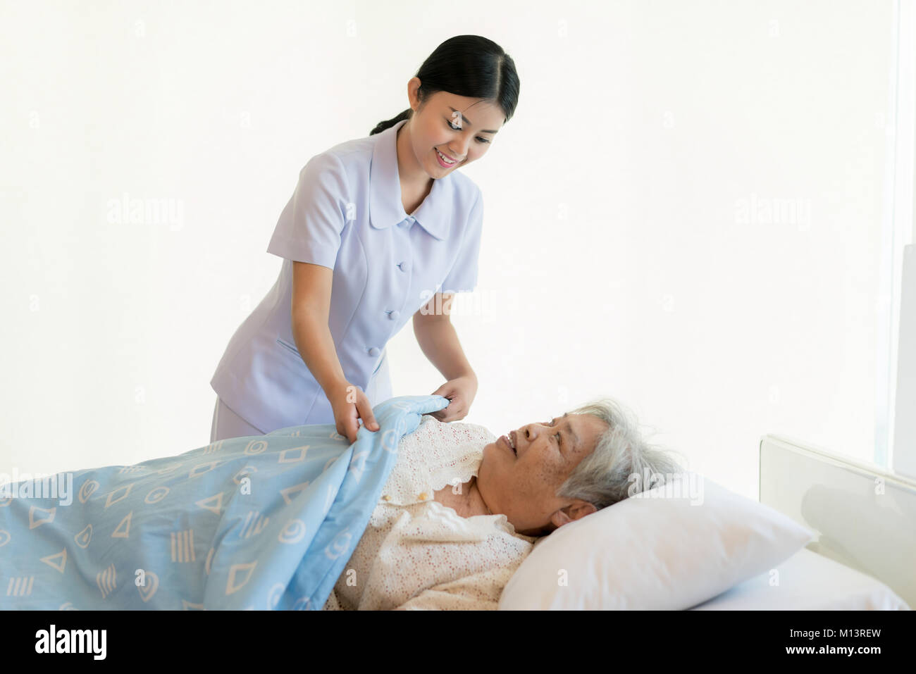 Asian infermiera in assistenza agli anziani coprirla con una coperta per gli anziani in casa di riposo. Foto Stock