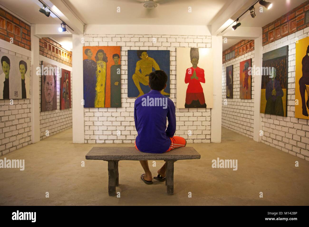 Cambogia, Battambang, uomo seduto su un banco di lavoro rivolta verso i dipinti della Galleria Romcheik 5 spazio d'arte Foto Stock