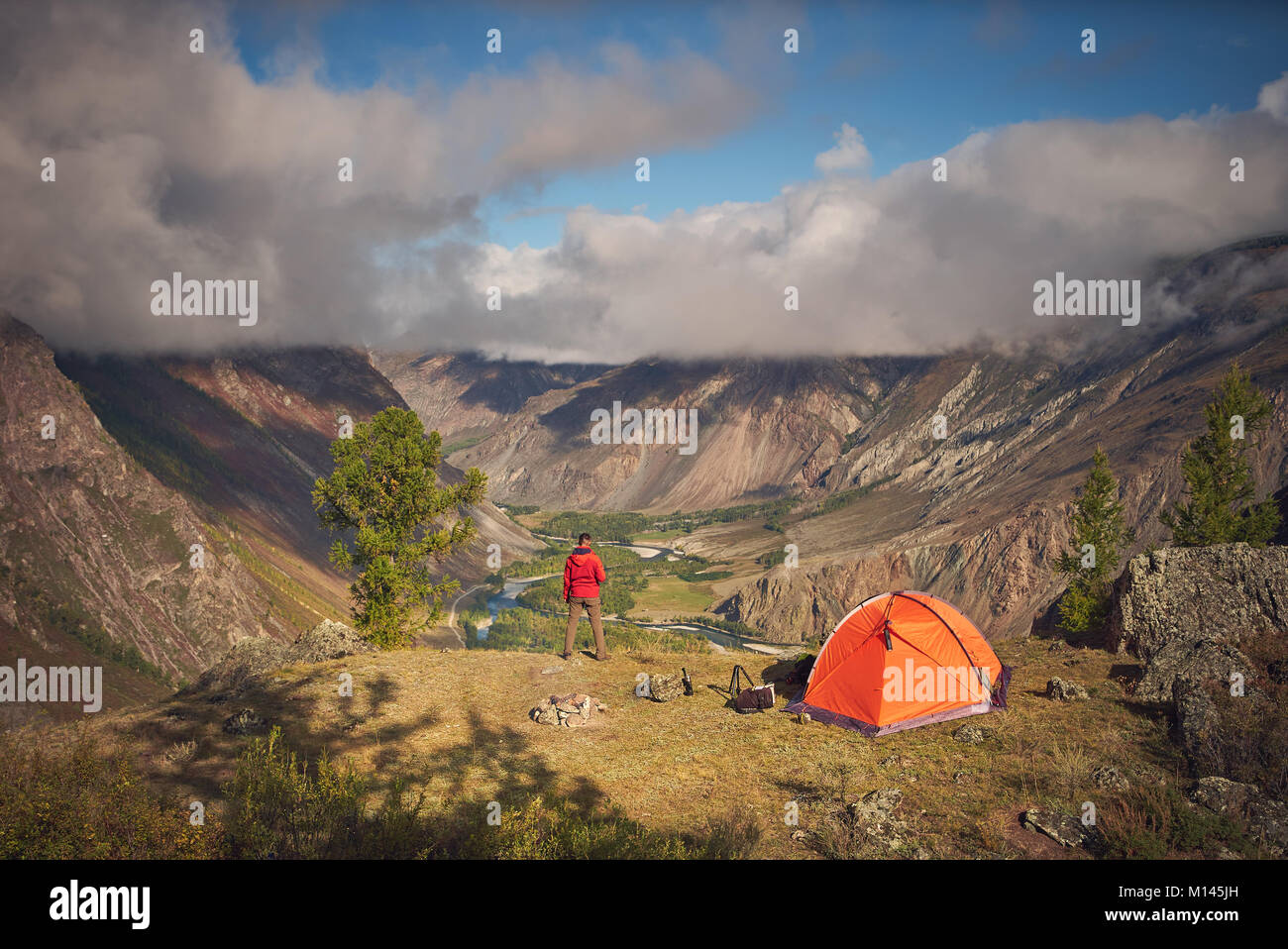 Persona che sorge nei pressi del campeggio e guardare la vista valle in cui vi è un fiume o di un ruscello e foresta. il cielo è nuvoloso, ma il tempo è sunn Foto Stock