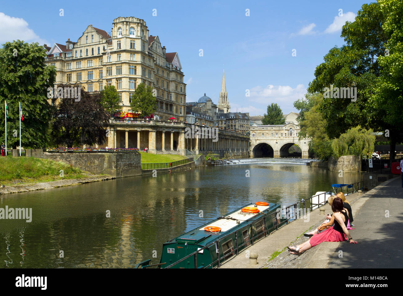 Bath, UK - 3rd luglio 2011: Donne che si trovano al sole estivo accanto alle colorate barche sul canale ormeggiate sul fiume Avon vicino al centro di Bath, Somerset, Regno Unito. Bath è un sito patrimonio dell'umanità dell'UNESCO famoso per la sua architettura. Foto Stock