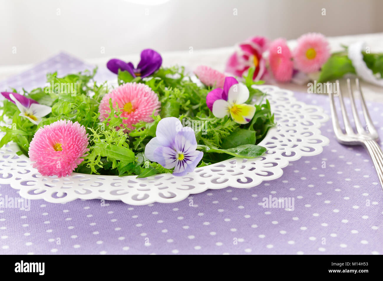 Piastra bianca con una insalata verde mista le foglie di lattuga e commestibile daisy e pansy fiori, insieme con una forcella di vintage su un nostalgico backgroun lilla Foto Stock