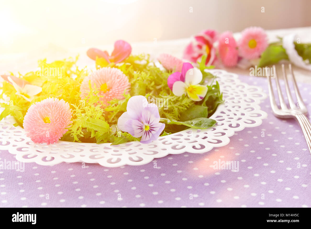 Piastra bianca con una insalata verde mista le foglie di lattuga e commestibile daisy e pansy fiori, insieme con una forcella di vintage su un nostalgico backgroun lilla Foto Stock