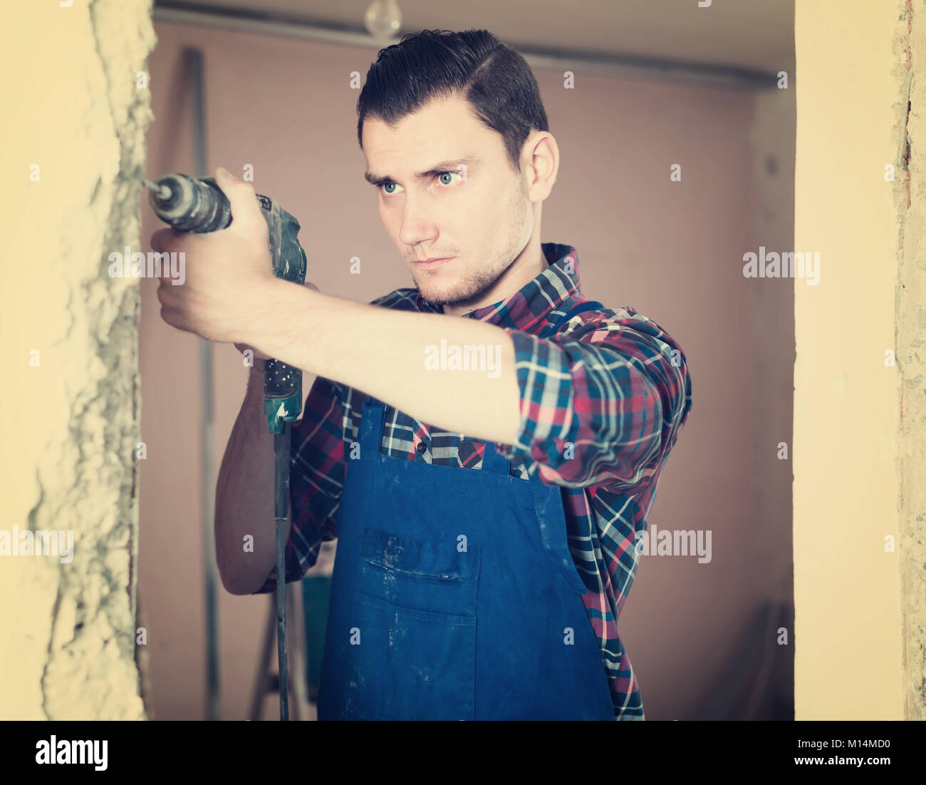 Calma professional builder foro di perforazione nella parete con un perforatore in una camera riparabile Foto Stock