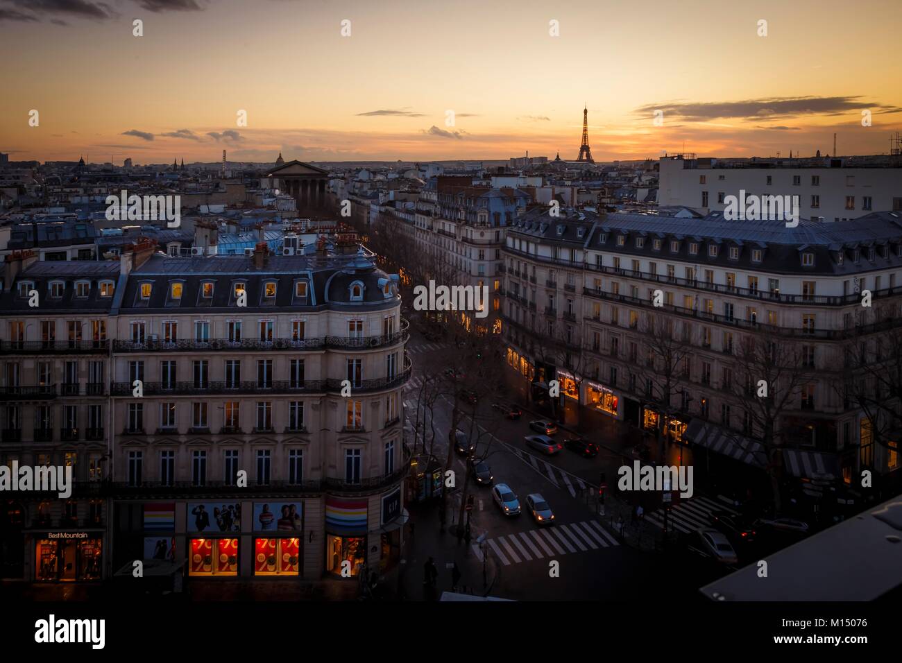 Vista in elevazione di un vivace viale di Parigi in Francia al tramonto con un bagliore arancione dal sole al tramonto nel cielo e una vista in lontananza la Torre Eiffel Foto Stock