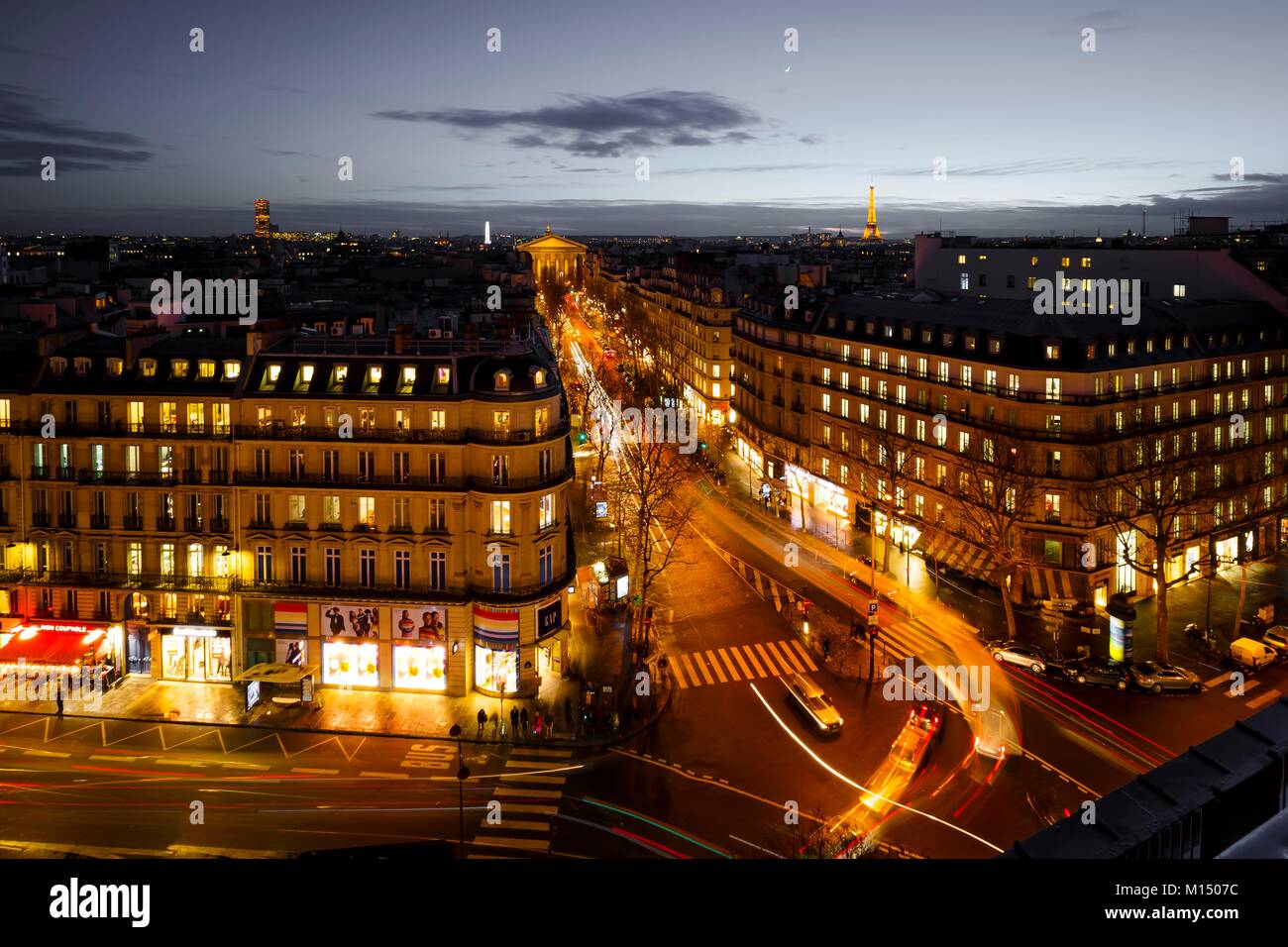 Via aerea in scena a Parigi di notte illuminata con edifici storici, negozi e una strada molto trafficata con percorsi di luce dal traf in movimento Foto Stock