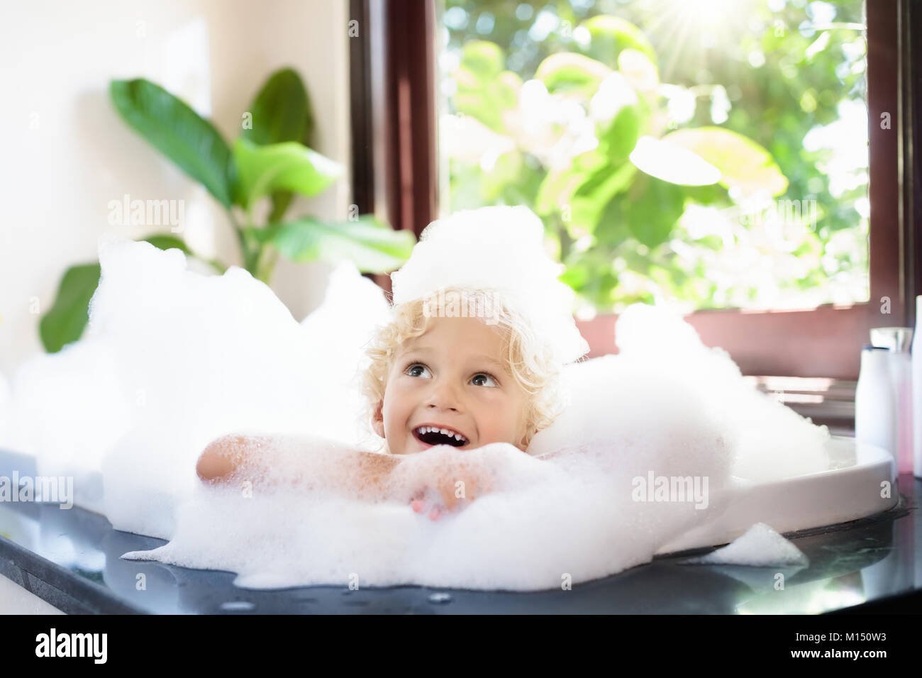 Bambino tenendo bagno di bolle in un bellissimo bagno con grande giardino  vista finestra. I ragazzi