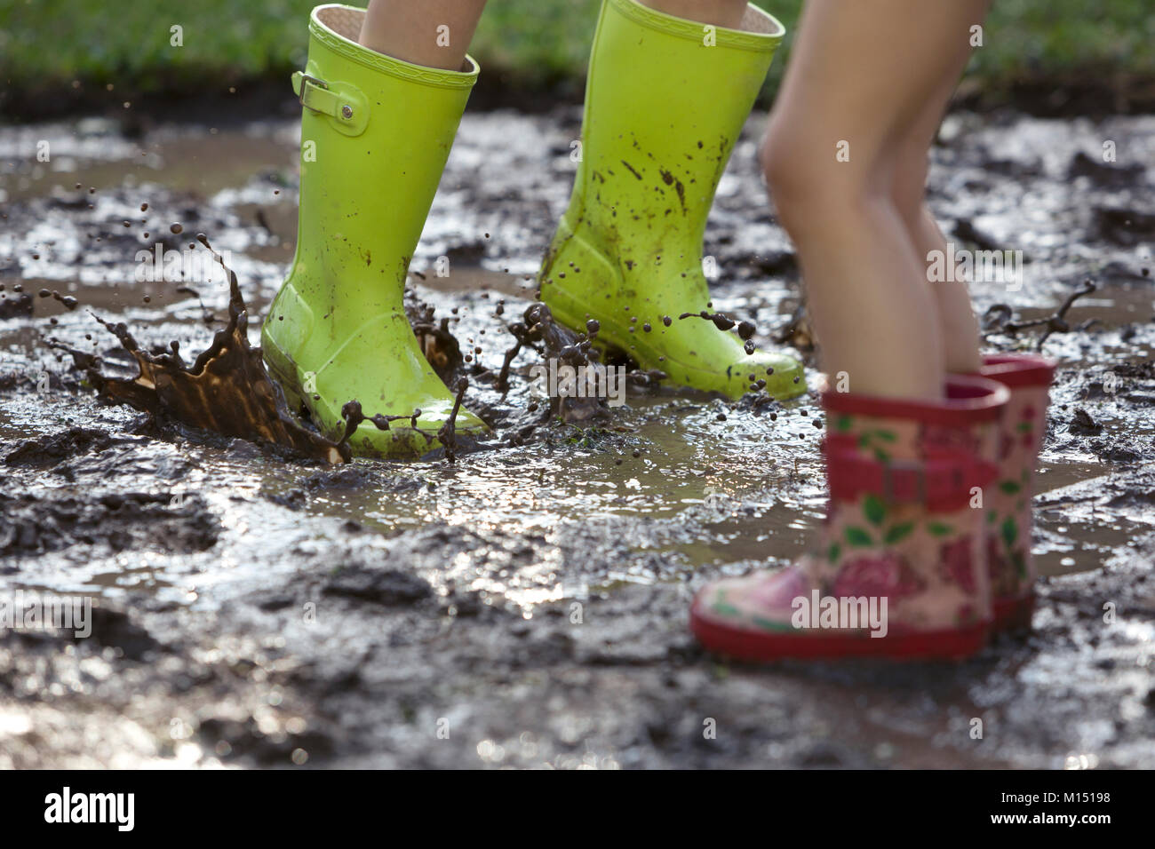 I bambini di saltare in una pozza di fango, indossare gli stivali da pioggia Foto Stock