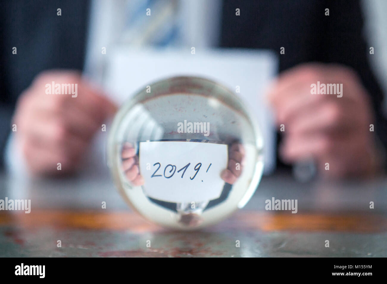 Primo piano dell'uomo tenendo la carta con i numeri 2019 davanti a sfera di vetro Foto Stock