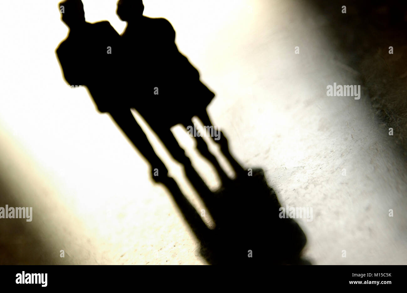 Due figurine di una coppia di anziani si avvicinano, proiettando ombre morbide su una superficie riflettente luminosa Foto Stock