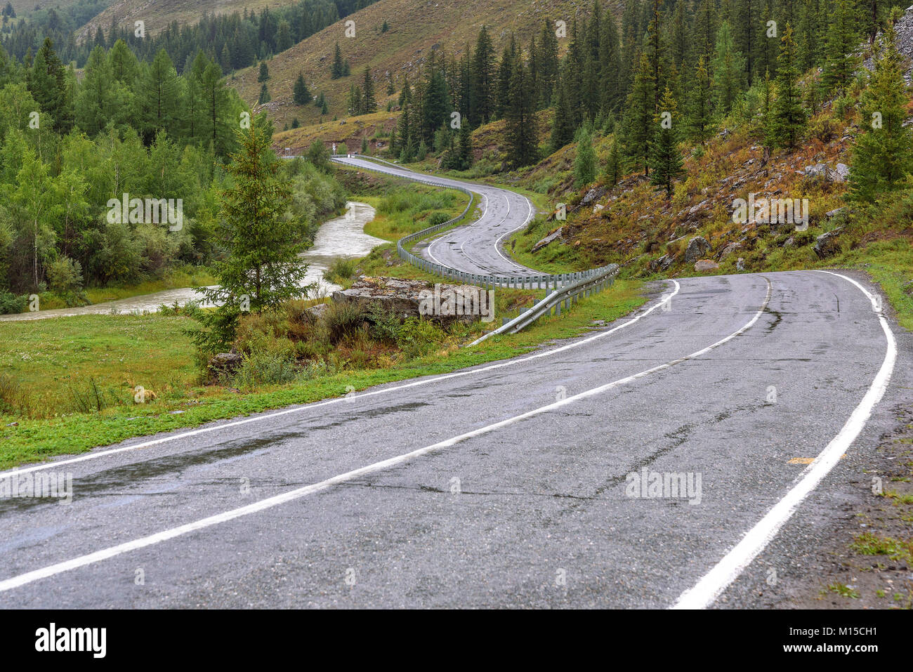 Vista panoramica con un avvolgimento umido strada asfaltata in montagna, nebbia, la foresta e il fiume in tempo nuvoloso Foto Stock