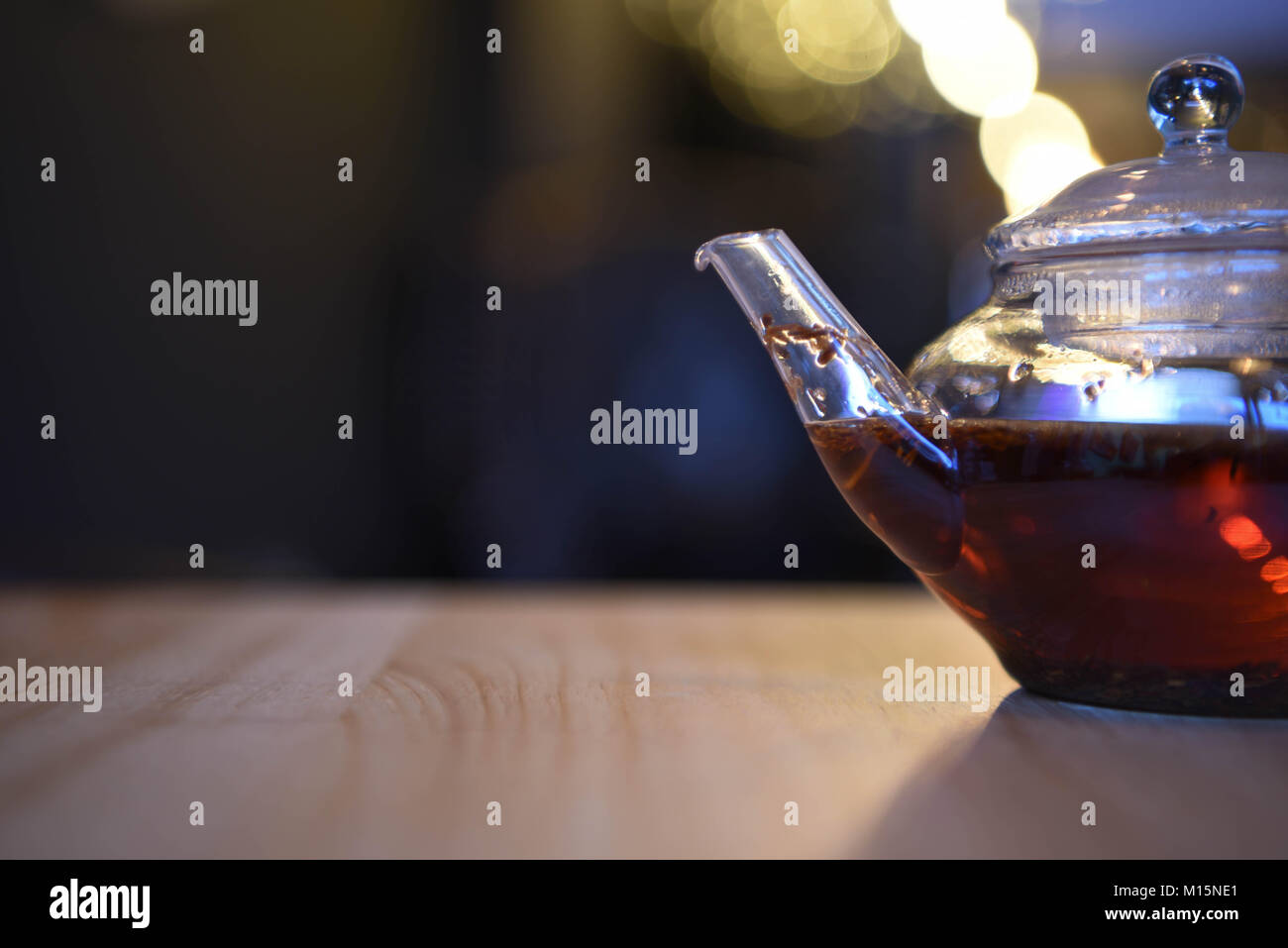 Immagine di bere un tè caldo realizzato in una teiera in vetro e con bokeh sfocato sfondo luminoso e tè aromatizzati con frutta fragola kiwi mela e spezie Foto Stock