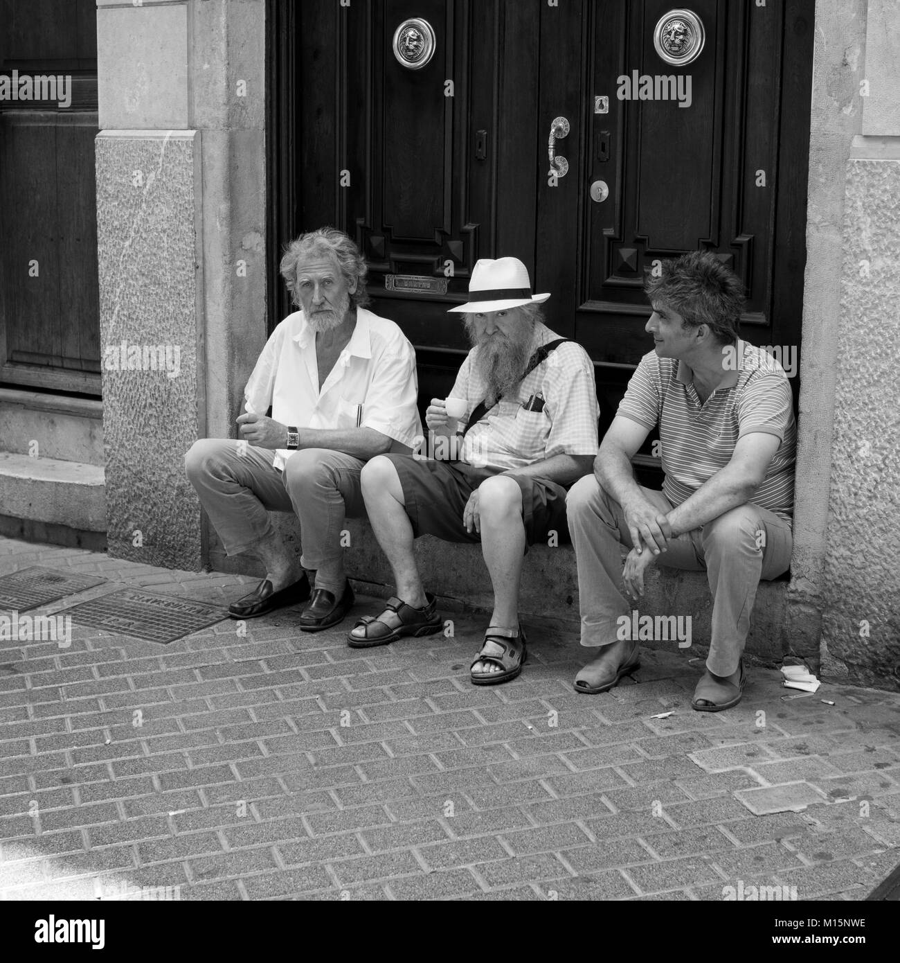 Tre amici di sedersi su un passo di davanti di vecchie porte in legno in una strada a Palma di Mallorca godendo di caffè e conversazione Foto Stock