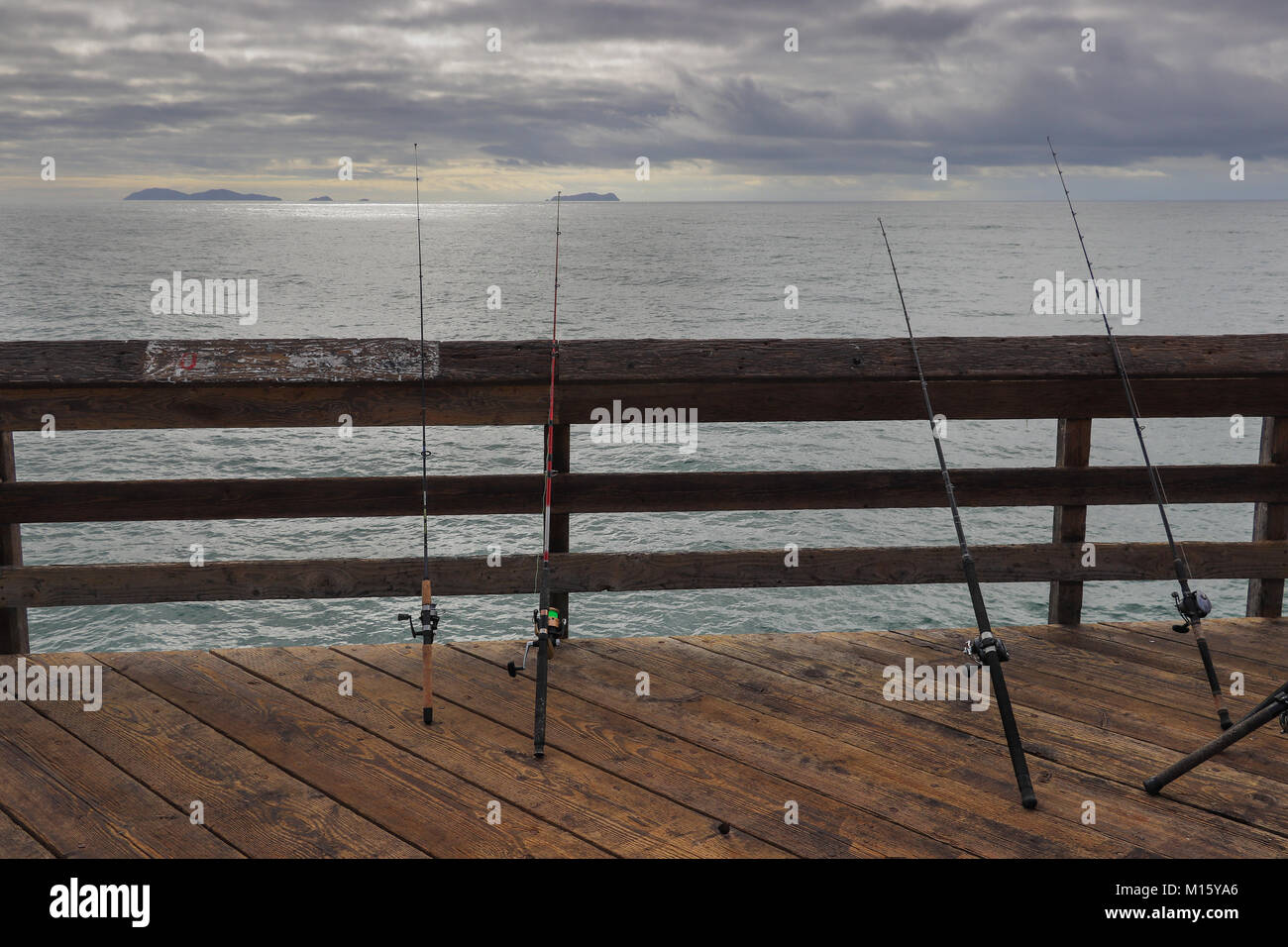 Quattro poli di pesca in appoggio sulla ringhiera della Imperial Beach Pier in California il giorno nuvoloso, l'Oceano Pacifico e le isole di Coronado in background Foto Stock
