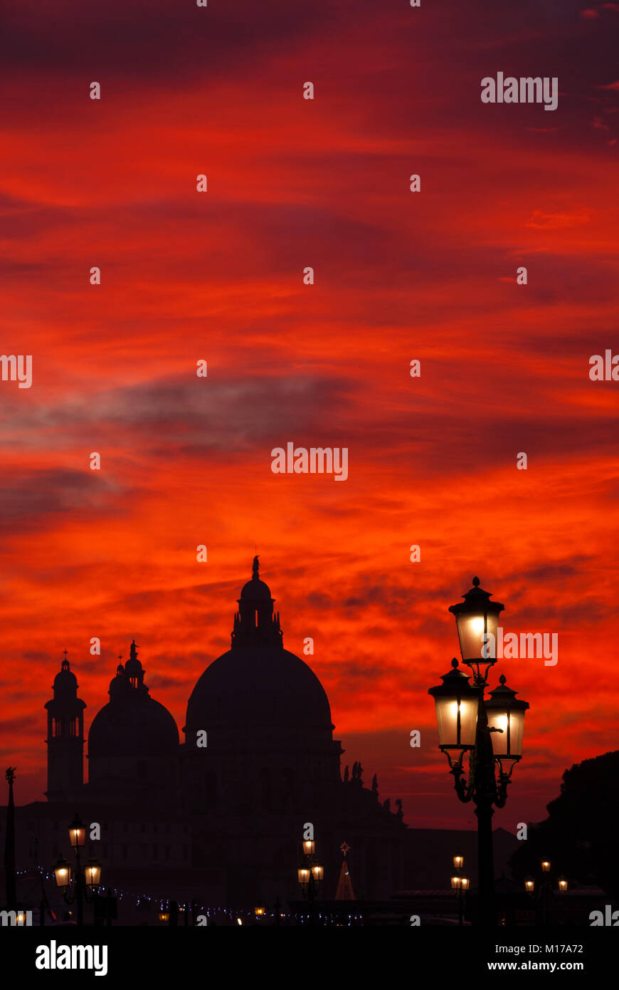 Rosso Sangue sky tramonto sulla laguna di Venezia con la Basilica salutano le cupole, San Marco Lion e lampade Foto Stock