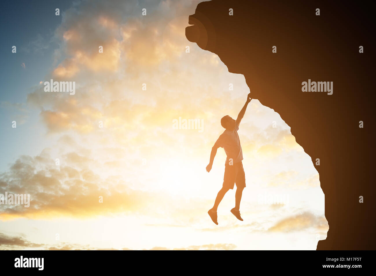 Silhouette di un uomo scalatore appesa sopra la roccia con la sua mano al tramonto Foto Stock