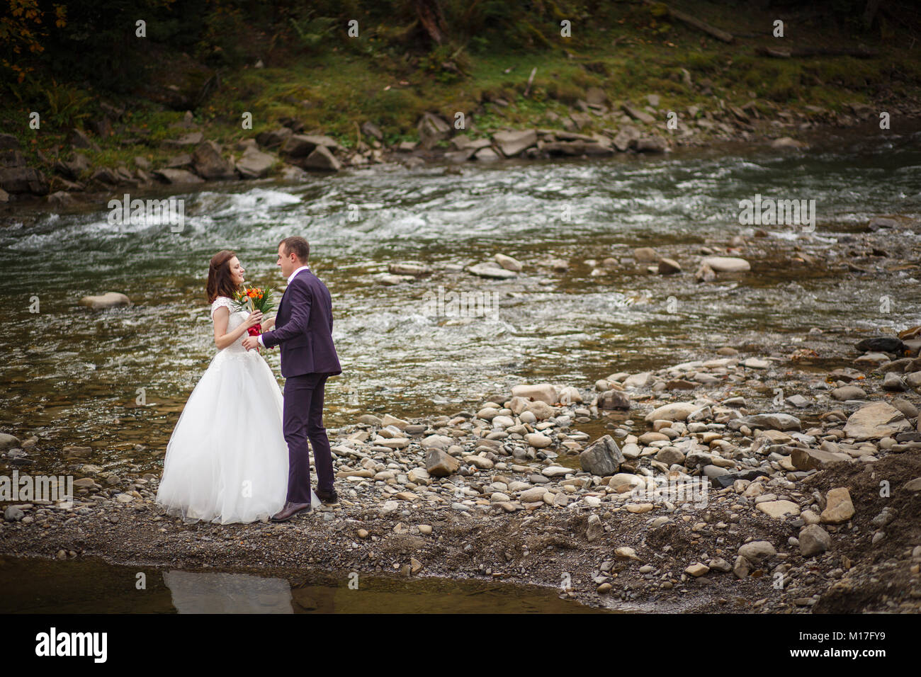 Sposa e lo sposo Passeggiate sul fiume, sorridente e baciare Foto Stock