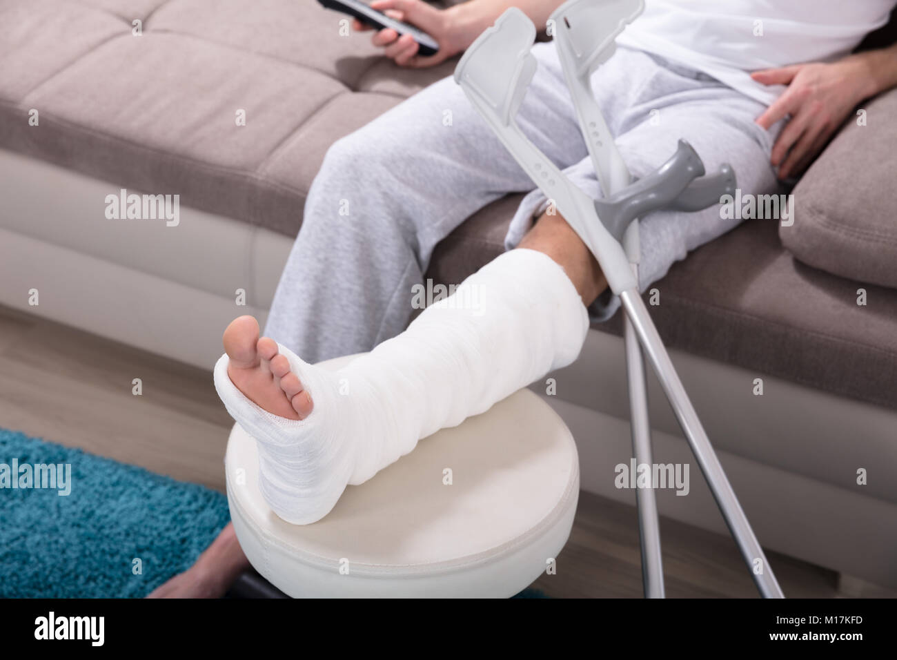 Giovane uomo Con gamba rotta seduti sul divano Azienda Remote Foto Stock