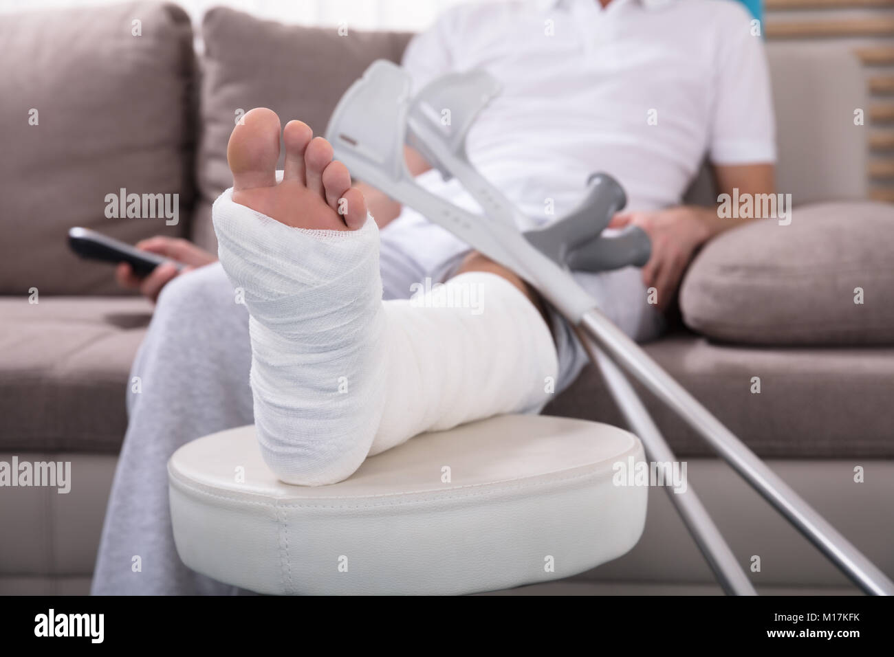 Giovane uomo Con gamba rotta seduti sul divano Azienda Remote Foto Stock