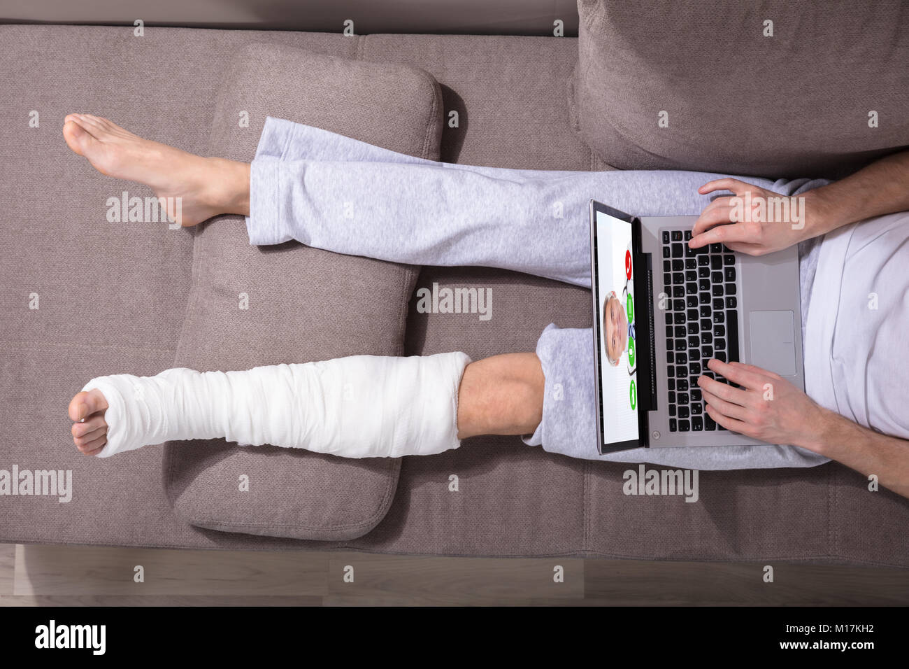 Elevato angolo di visione di un uomo con la gamba intonacata Videoconferenza con il medico su Laptop Foto Stock