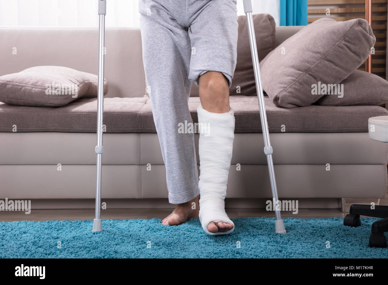 Giovane uomo Con gamba rotta usando stampelle per alzarsi dal divano Foto Stock