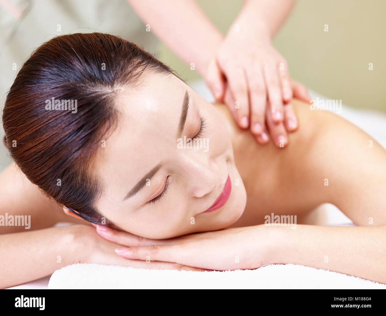 Close-up del volto di una giovane e bella donna asiatica che giace sulla parte anteriore sul letto ricevente in massaggio spa salone. Foto Stock