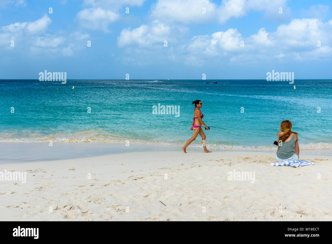 Oranjestad, Aruba - Gennaio 4, 2018: un turista rilassarsi nell'idilliaco Eagle Beach ad Aruba mentre una donna a piedi sulla riva. Foto Stock