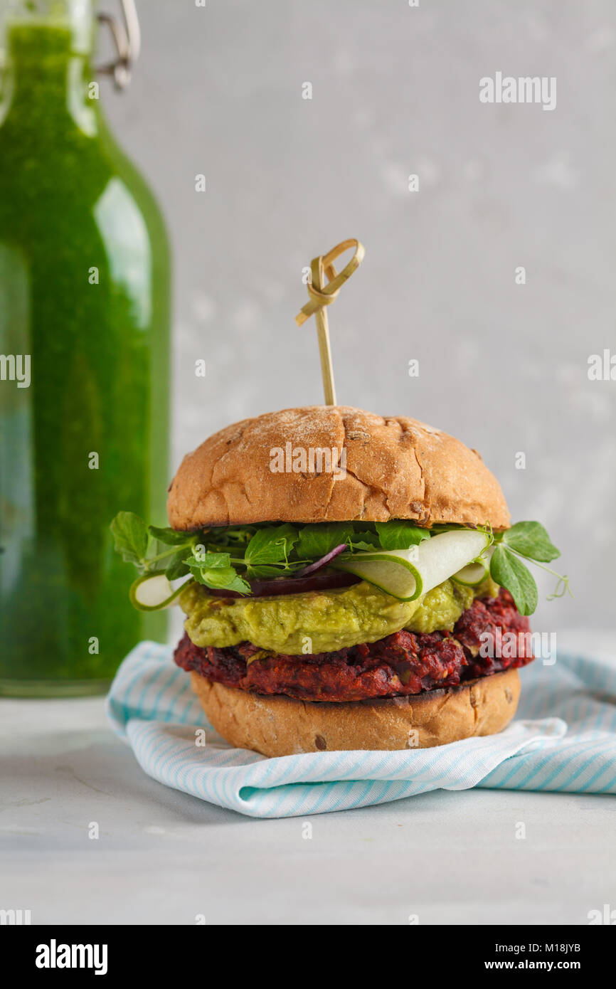 Vegan burger di barbabietole con verdure, guacamole e segala bun con verde frullato. Sano cibo vegan concetto. Foto Stock